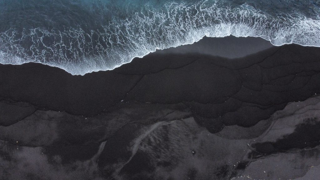 Luftaufnahme eines schwarzen Sandstrandes im Norden der Insel Bali in Indonesien.